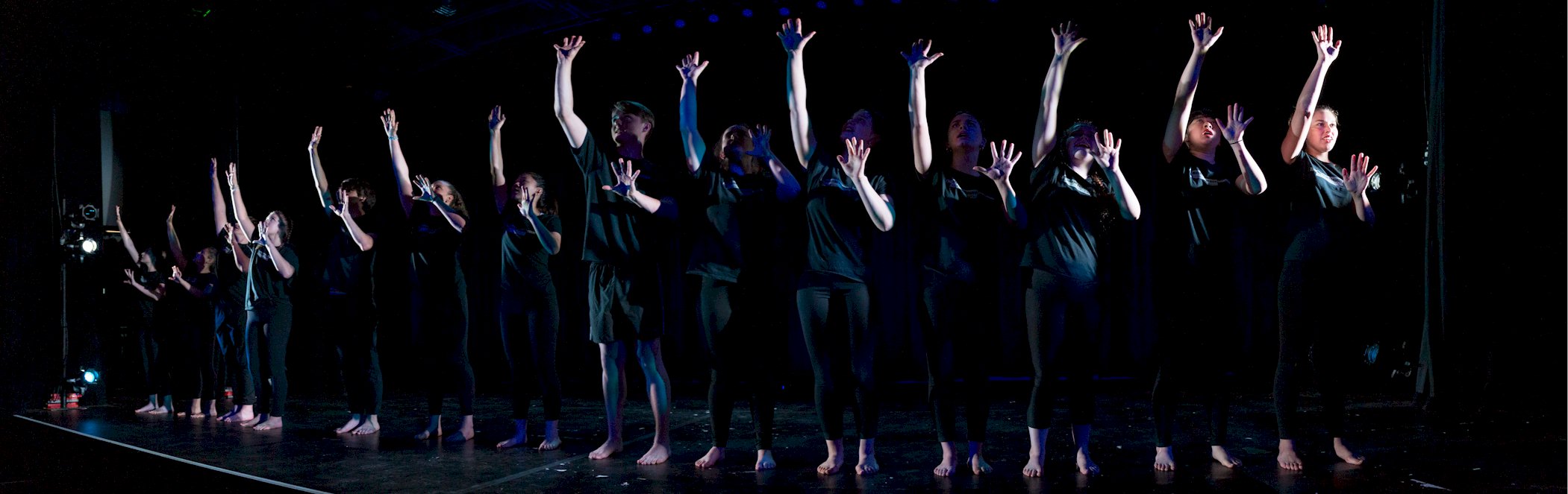 Photo of young artists in black clothing performing on a dimly lit stage.